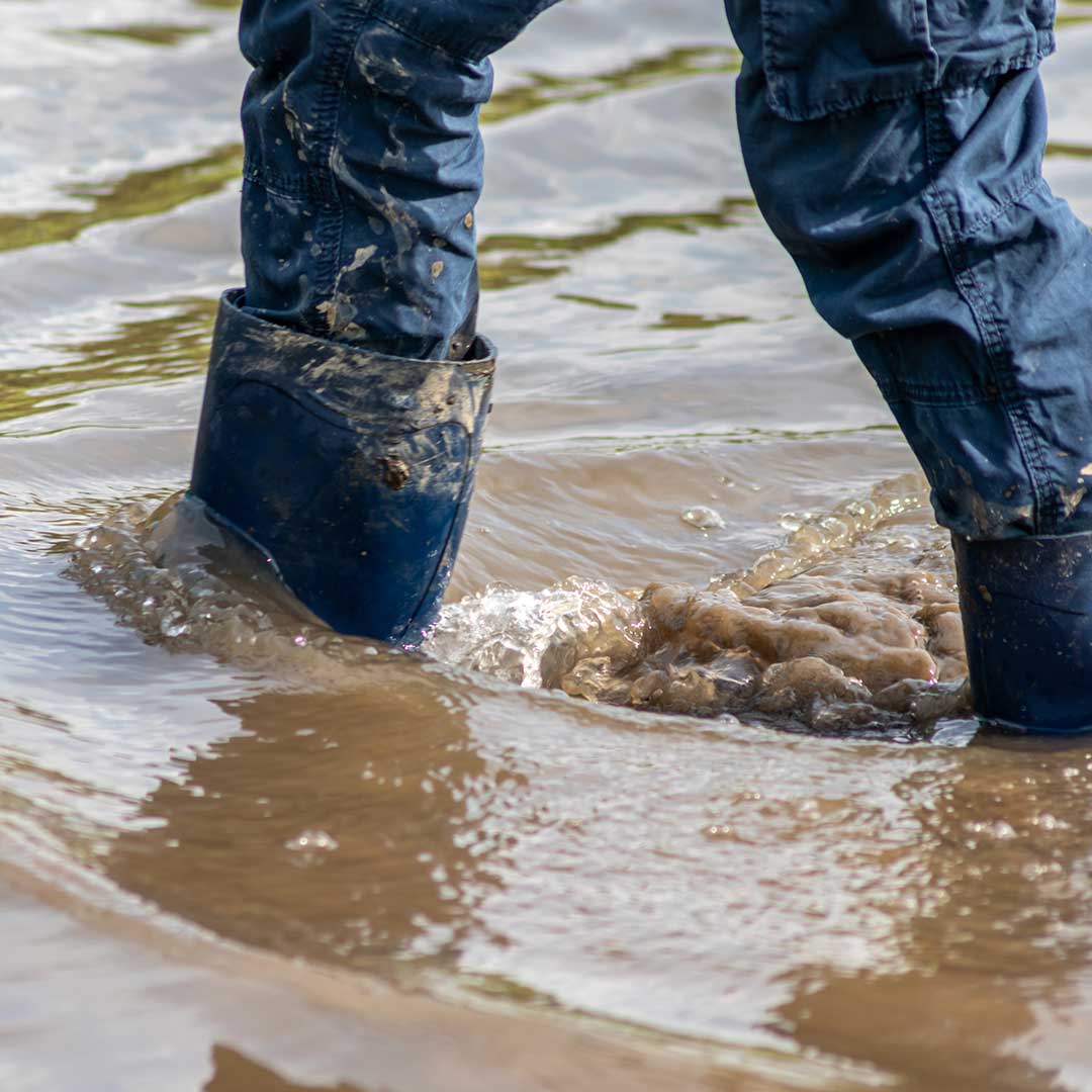 Person mit Gummistiefel in hohem dreckigem Wasser