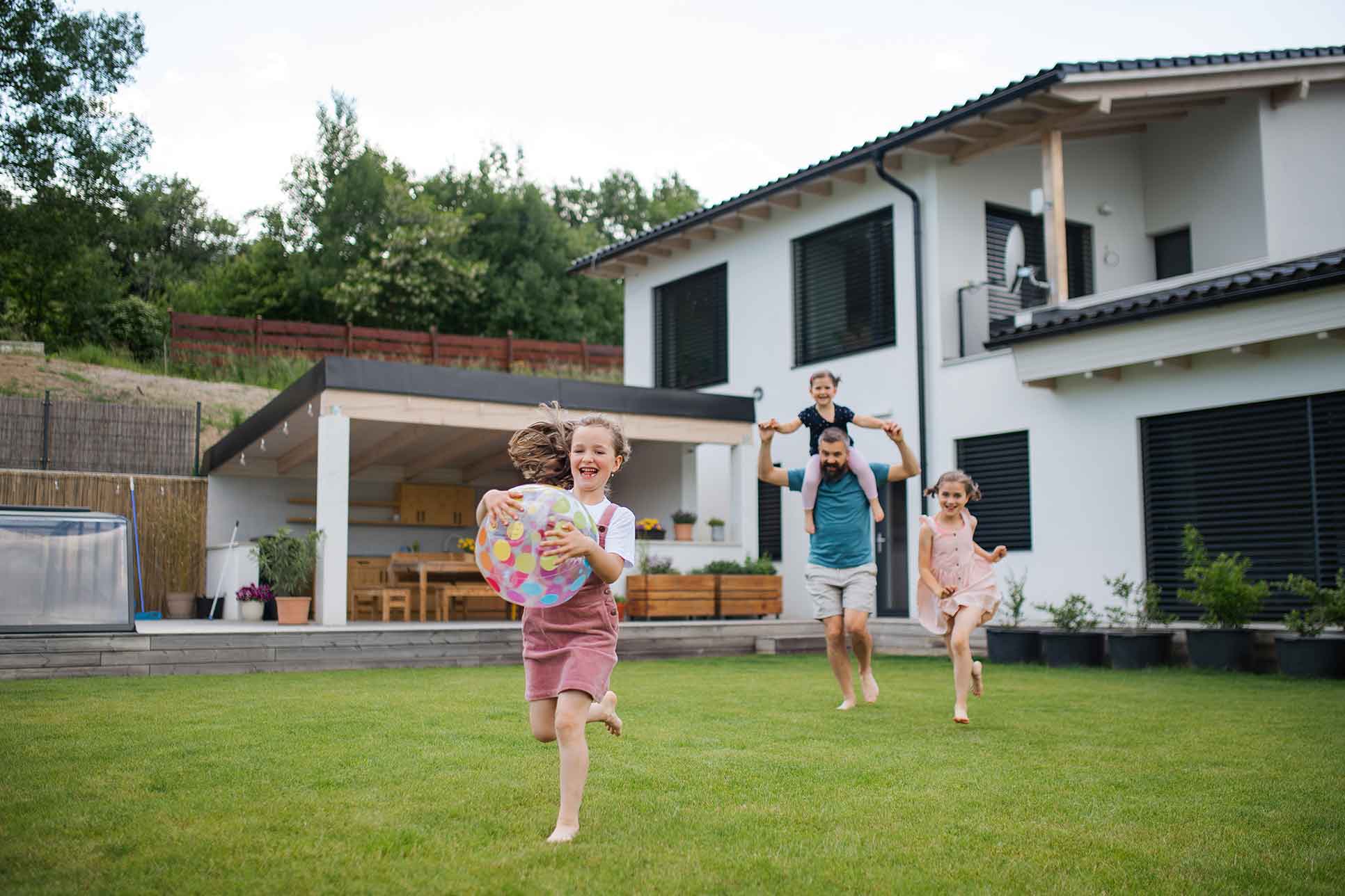 Garten eines Wohnhauses, in dem ein Vater mit seinen Kindern spielt