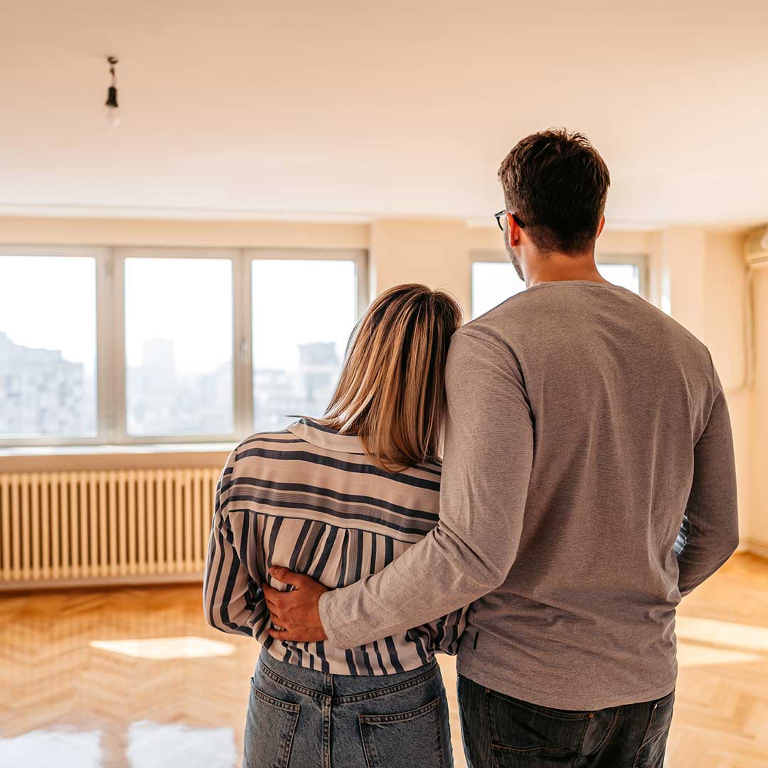 Ein Paar betrachtet gemeinsam eine leere Wohnung mit großen Fenstern.