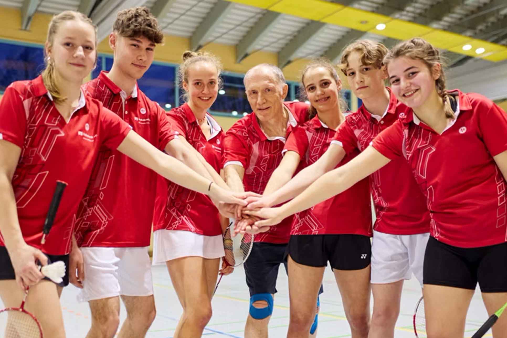 Eine Gruppe aus Badminton Spieler:innen in roten Trikots