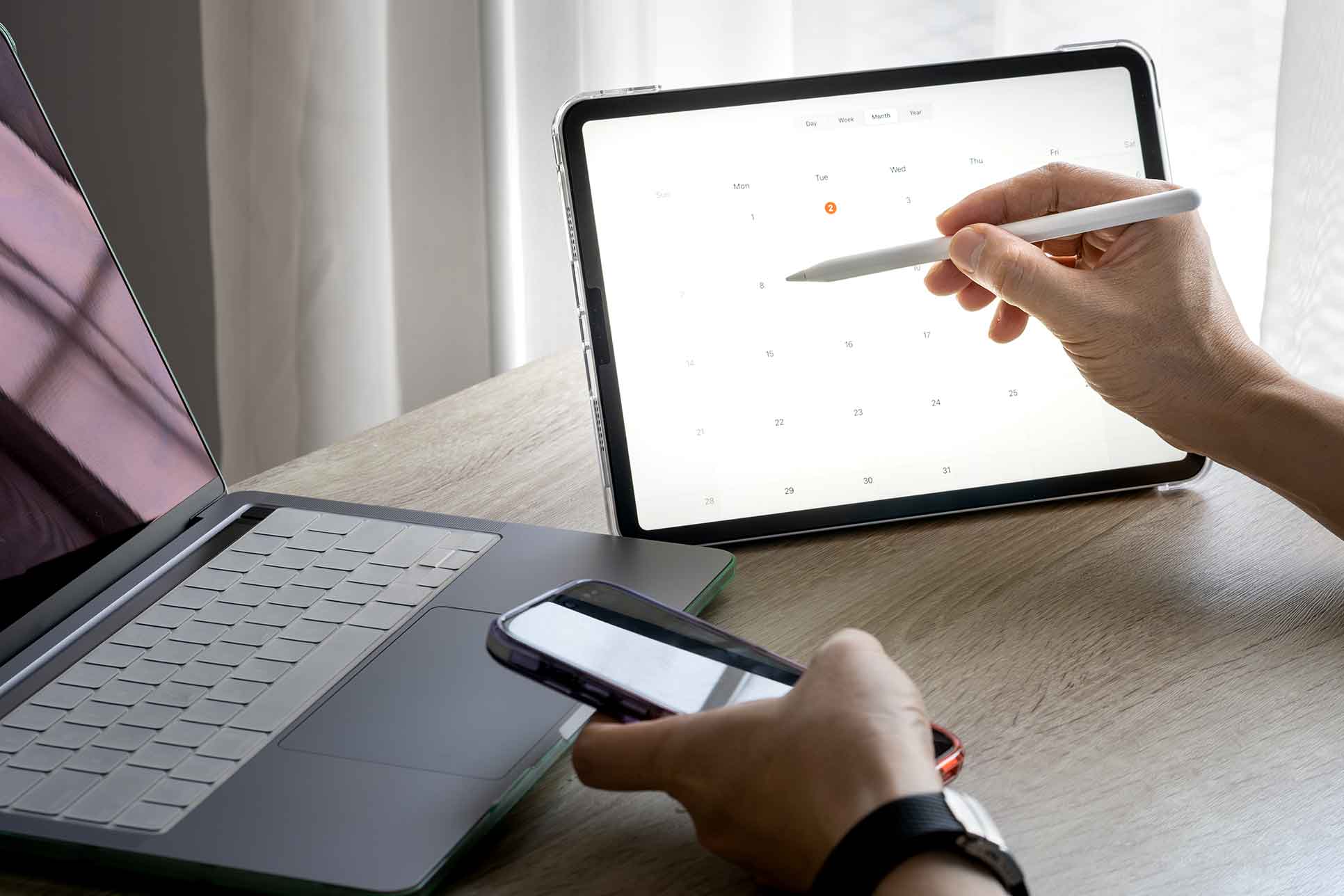 Nahaufnahme zweier Hände. Die eine Hand hält ein Smartphone und die andere bedient ein iPad.
