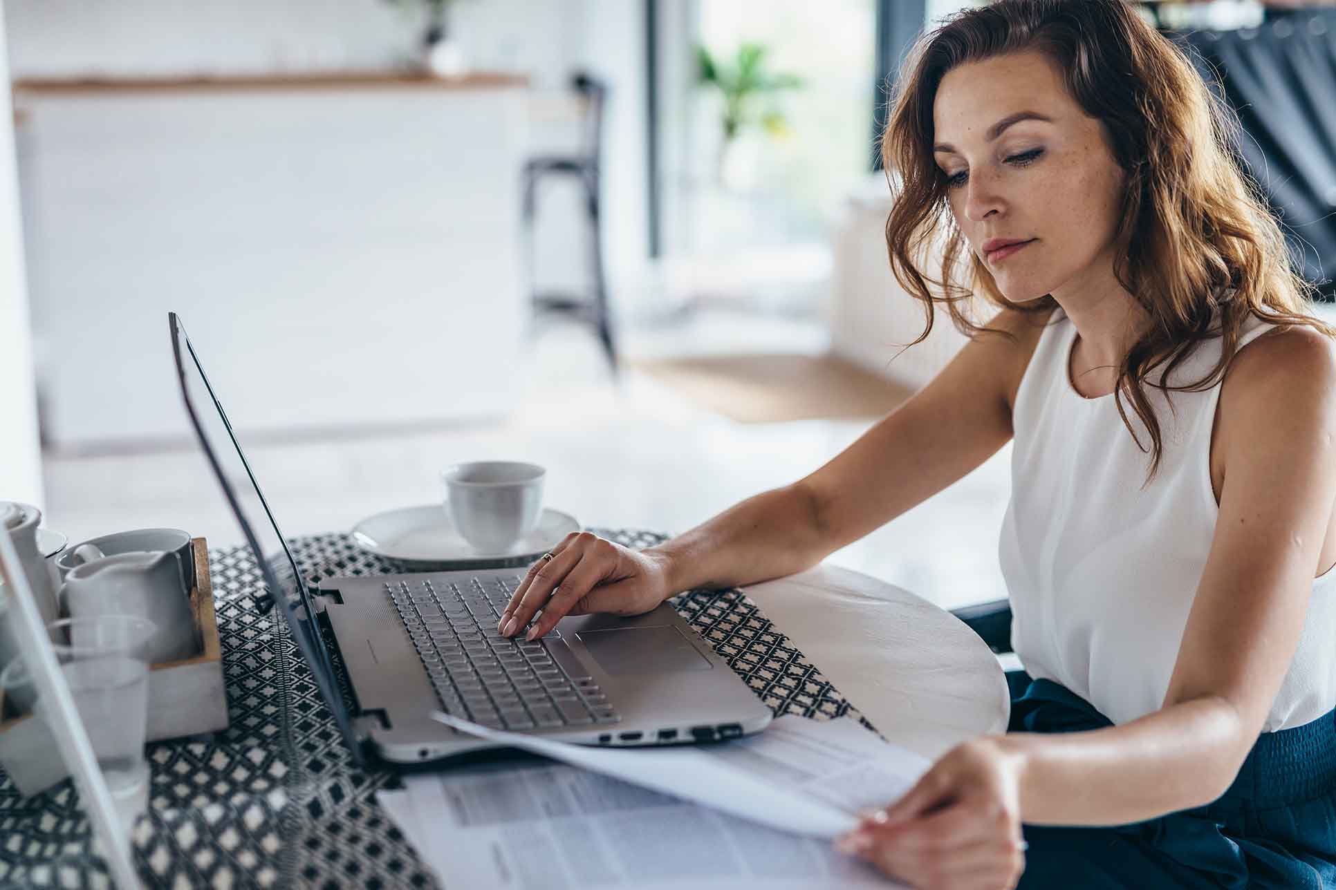 Eine Frau sitzt vor ihrem Laptop und hält ein Dokument in ihren Händen