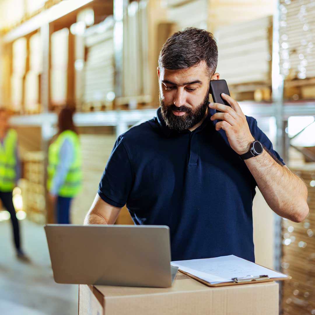 Ein Mann steht in einem Lager und prüft Bestellungen an seinem Laptop