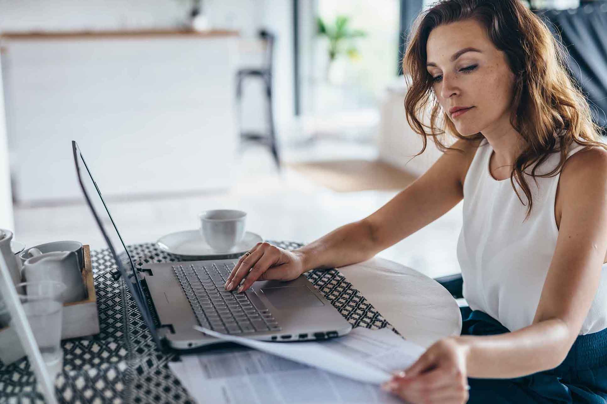 Eine Frau sitzt vor einem Laptop und hält Dokumente in der Hand